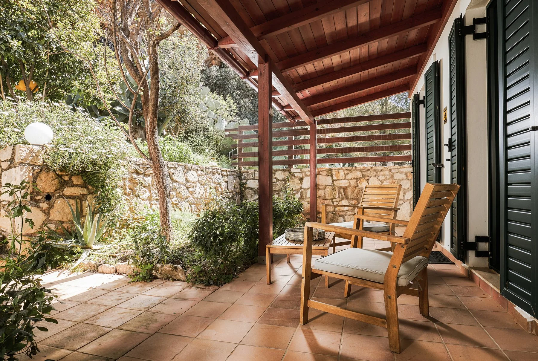 Shaded patio with wooden chairs and garden plants at Yiamas Seaside Cottage
